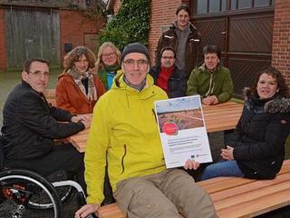 Eine Gruppe von Personen und ein Mann im Rollstuhl sitzen gemeinsam an einer unterfahrbaren Picknick-Sitzgruppe.