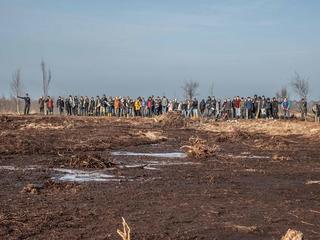 Eine große Gruppe Schülerinnen und Schüler hat sich in einem Moor für ein Gruppenbild zusammengestellt. Einige halten junge Bäume und Äste hoch.