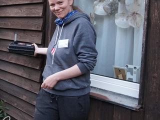 Eine Frau steht vor einer Holzfassade und hält einen Fledermausdetektor an die Fassade.