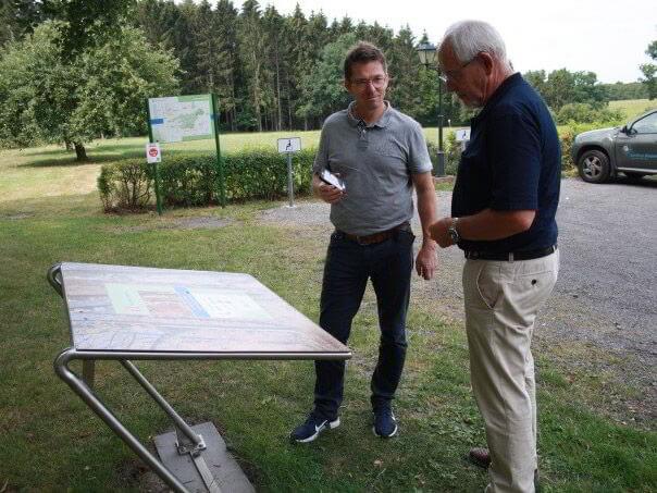 Zwei Personen stehen vor einer Hörtafel und hören sich die Informationen zur Sehenswürdigkeit auf dem Smartphone an.