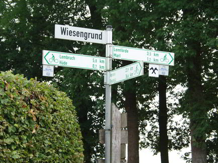 Ein Straßenschild mit drei Wegweisern für Fahrradfahrer – mit Kilometer-Angaben zu unterschiedlichen Orten.
